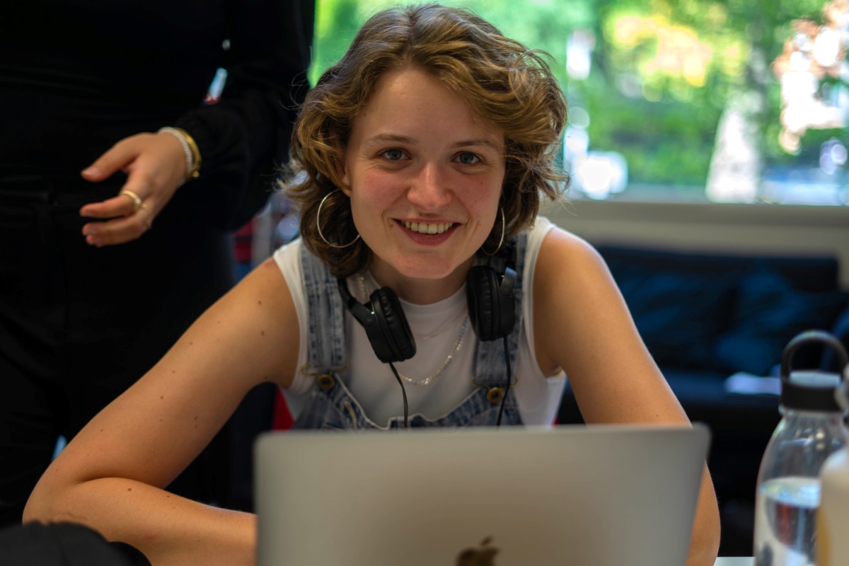 Junge Frau an einem Laptop, trägt Kopfhörer und lächelt.