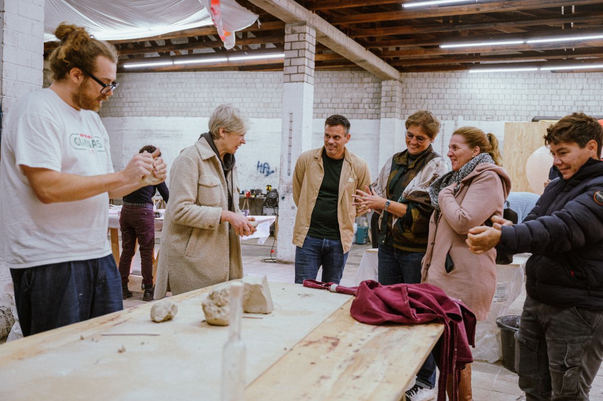 Ein Mitarbeiter der S27 erklärt Mitarbeitenden der Neuguss Gruppe das Arbeiten mit Ton, alle haben ein Stück Ton in der Hand und stehen um einen Tisch herum.