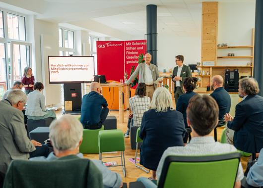 Mitarbeitende bei einer Mitgliederversammlung der GLS Treuhand, Vorstände stehen vorne und sprechen