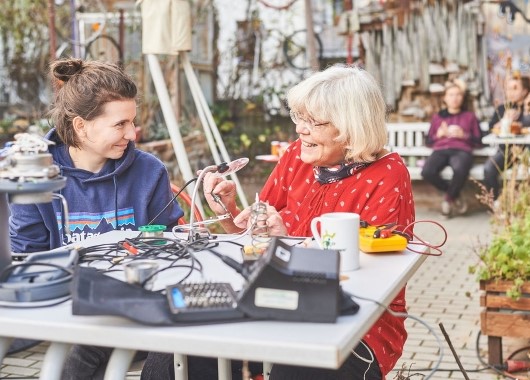 Café kaputt Leipzig, Zwei Frauen (eine jünger, eine älter) im Gespräch beim Reparieren im Hof
