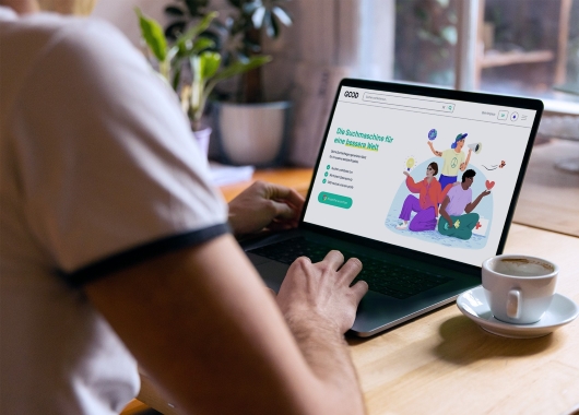 GOOD Search im Browser eines Laptops geöffnet, Mensch der am Laptop an einem Tisch sitzt.