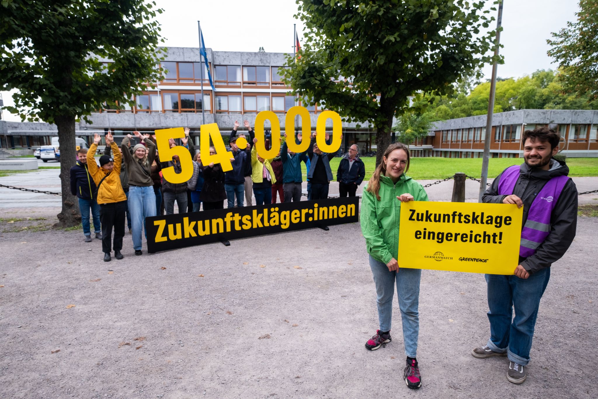 Untertstützer*innen halten die Zahl 54.000 hoch sowie das Wort "Zukunftskläger*innen" und ein gelbes Plakat auf dem steht "Zukunftsklage eingereicht" 