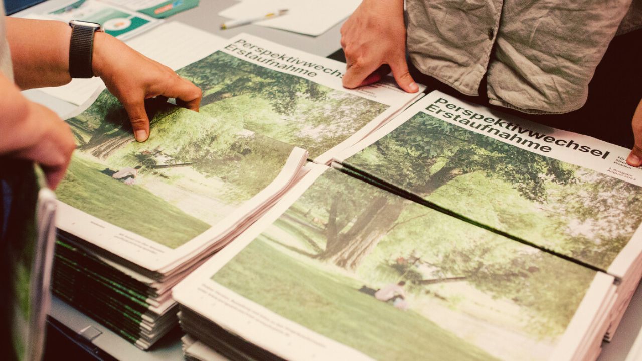 Menschen nehmen sich die Zeitung "Erstaufnahme Perspektivwechsel" mit