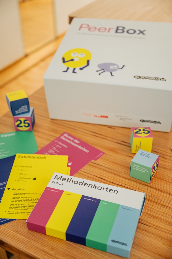 Bunte Lehrmaterialien der Zukunftsstiftung Bildung liegen auf einem Tisch aus. Zum Beispiel Methodenkarten und eine "Peer Box".