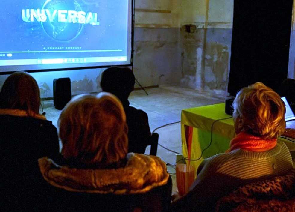 Man sieht das Publikum von hinten auf die Leinwand schauen