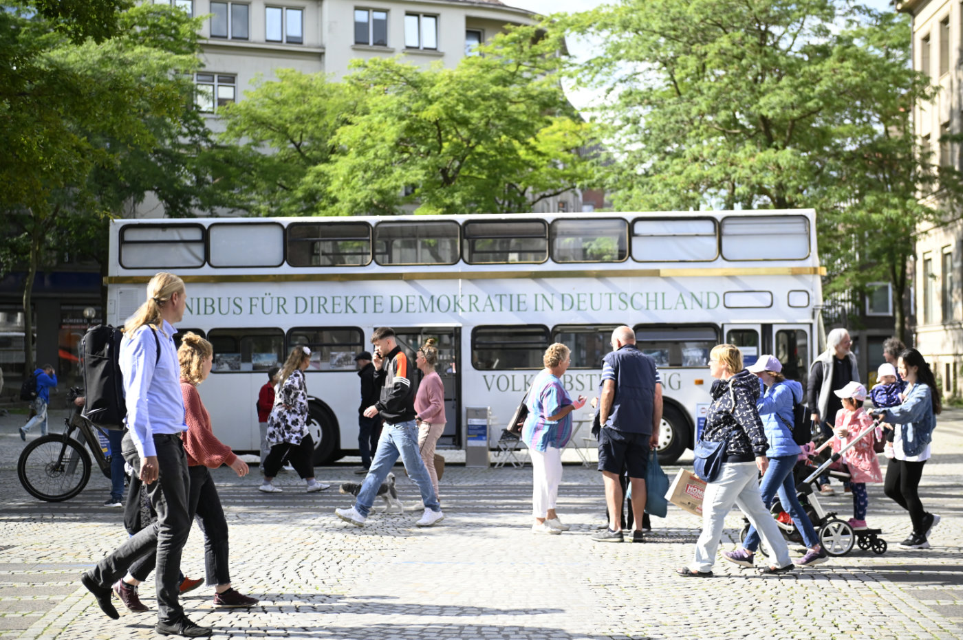 Bild vom Omnibus für Direkte Demokratie: Ein weißer Doppeldecker-Bus, davor Menschen.