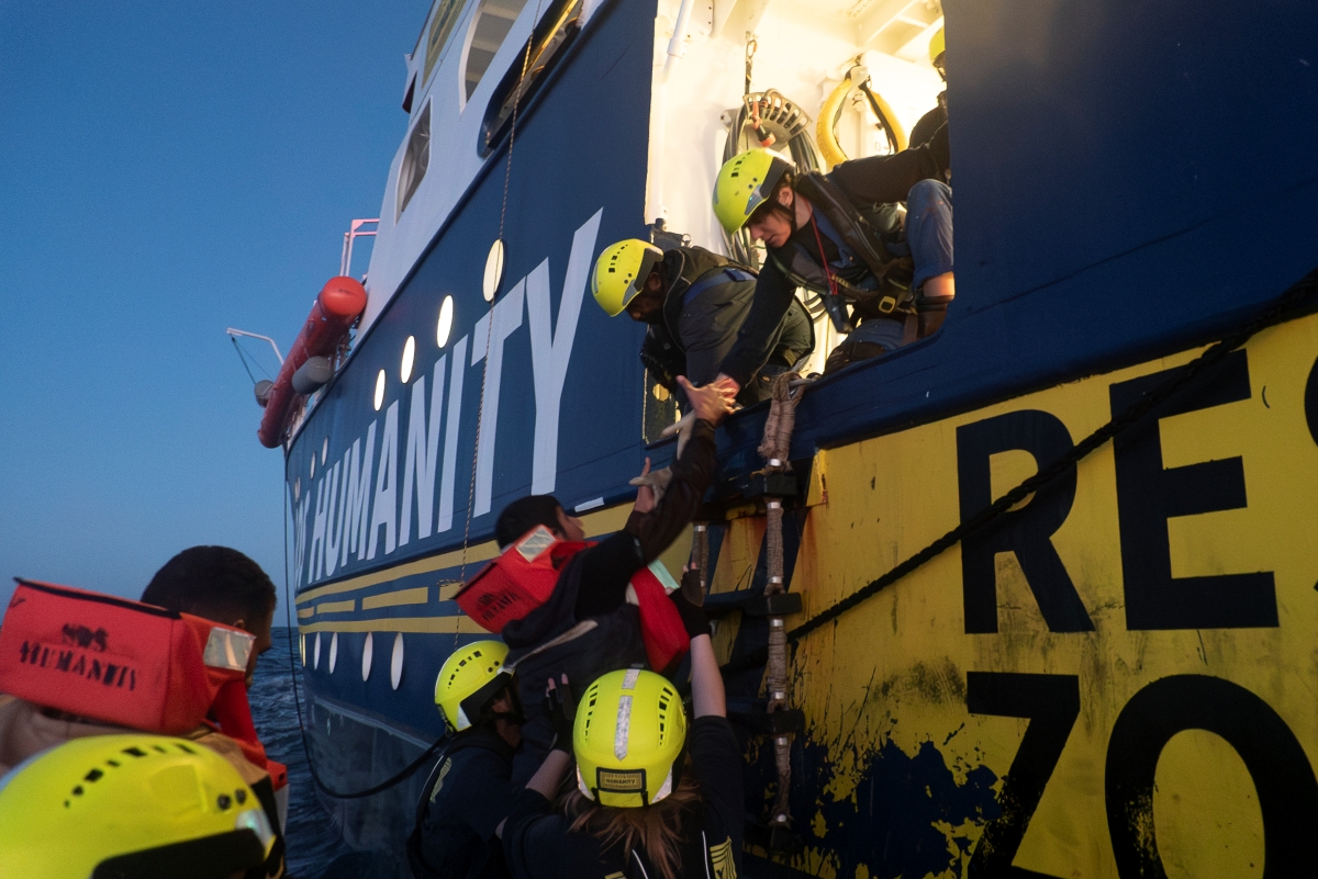Seenotretter*innen ziehen Menschen in Schwimmwesten an Bord