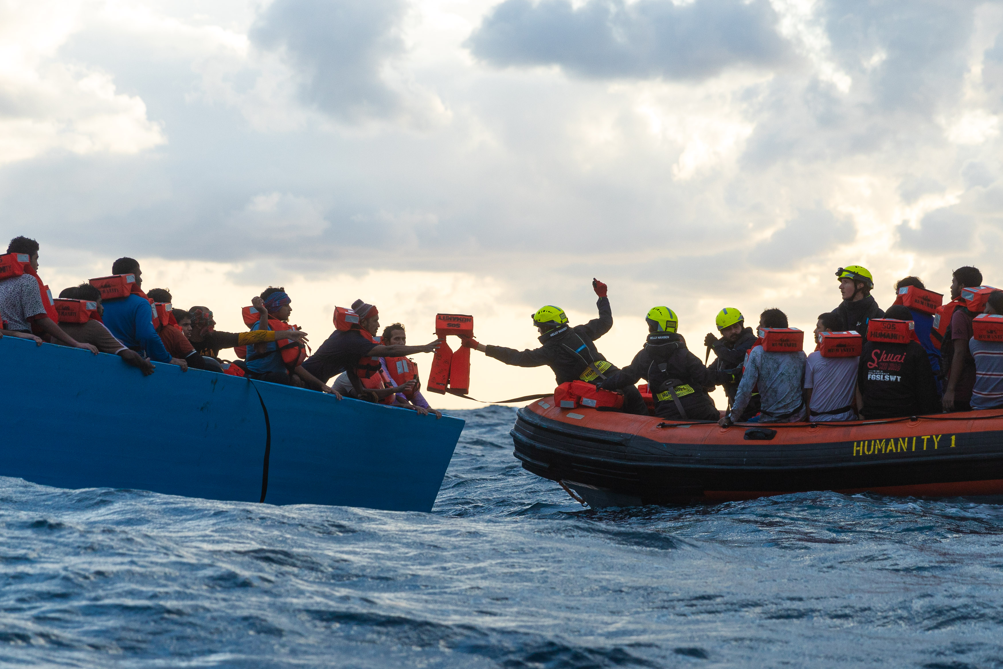 Seenotretter*innen reichen Menschen auf einem Boot Rettungswesten