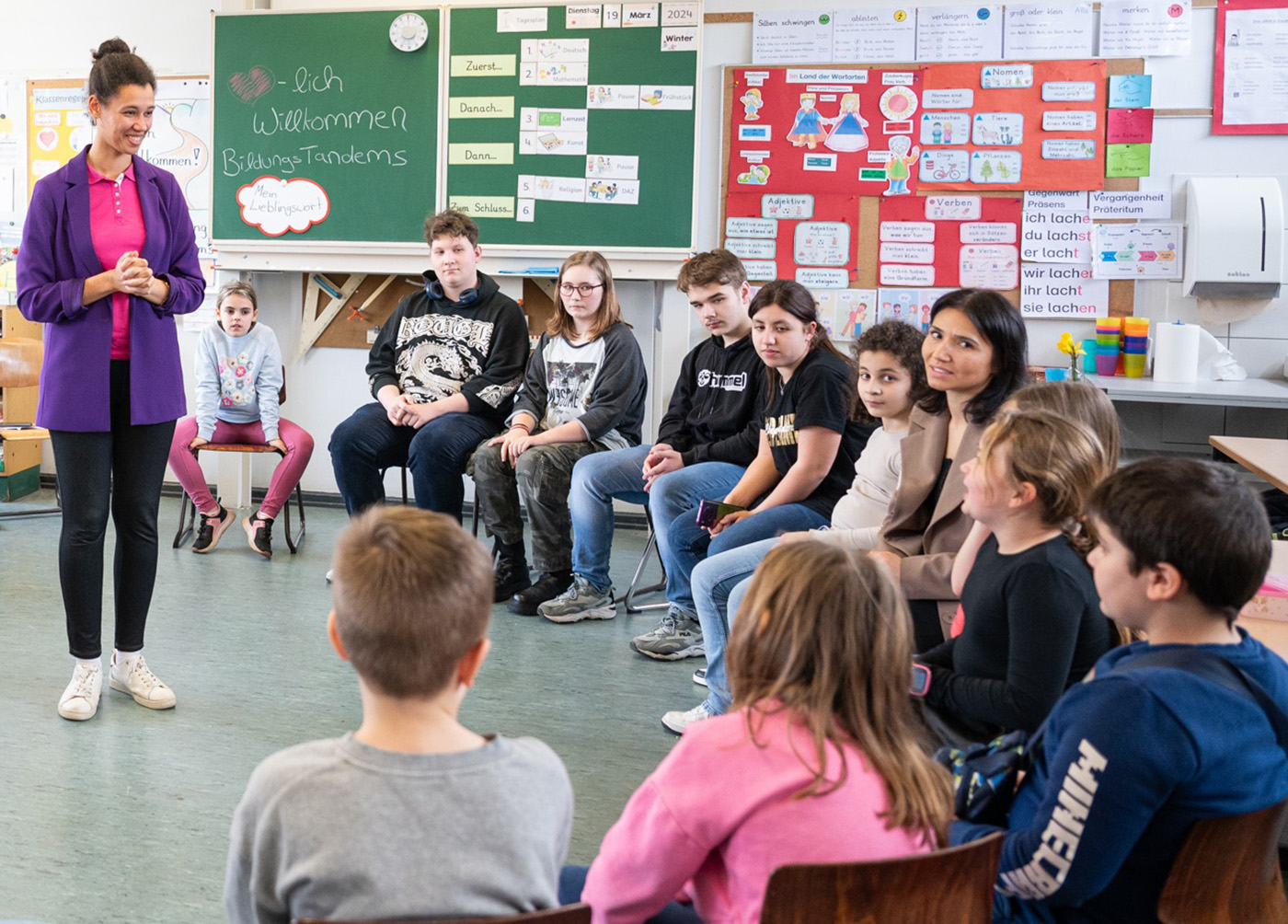 Eine Mitarbeiterin der Zukunftsstiftung Bildung steht vor einer Grundschulklasse und lächelt einem Mädchen zu