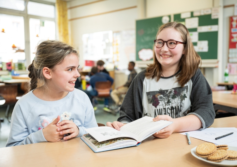Eine jüngere und eine ältere Schülerin schauen gemeinsam in ein Buch