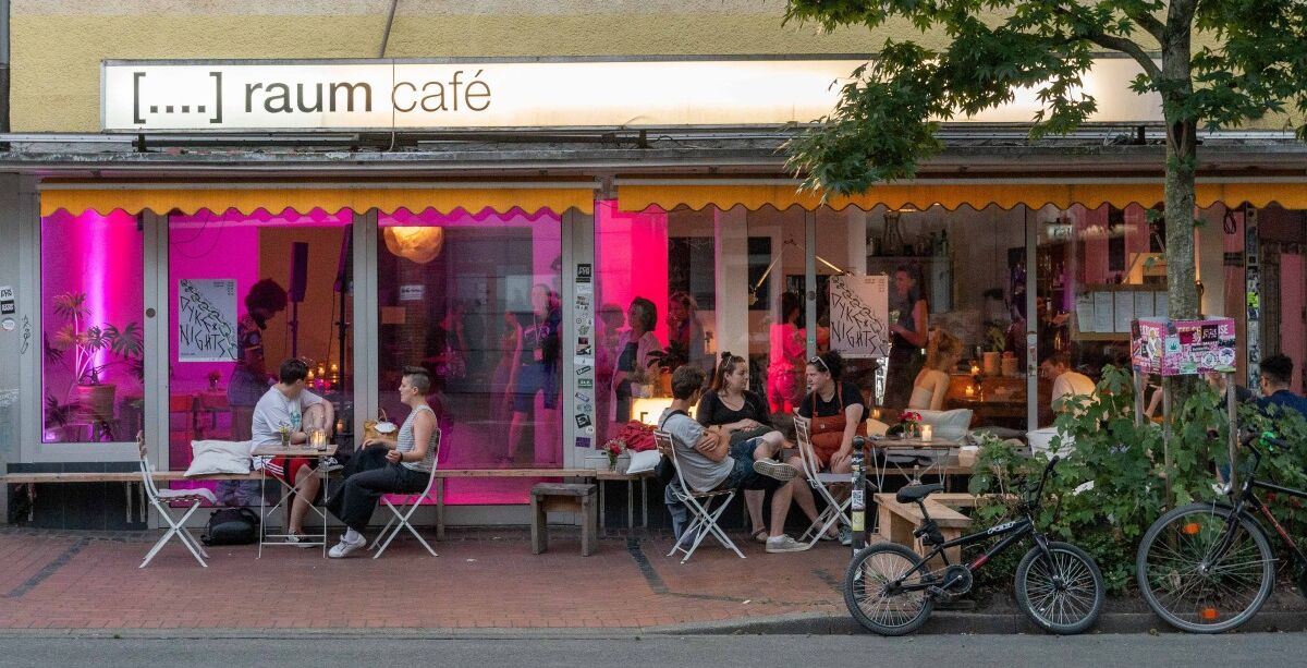 Außenansicht des raum cafés in der Wiesenstraße in Witten. Davor sitzen junge Menschen und unterhalten sich.
